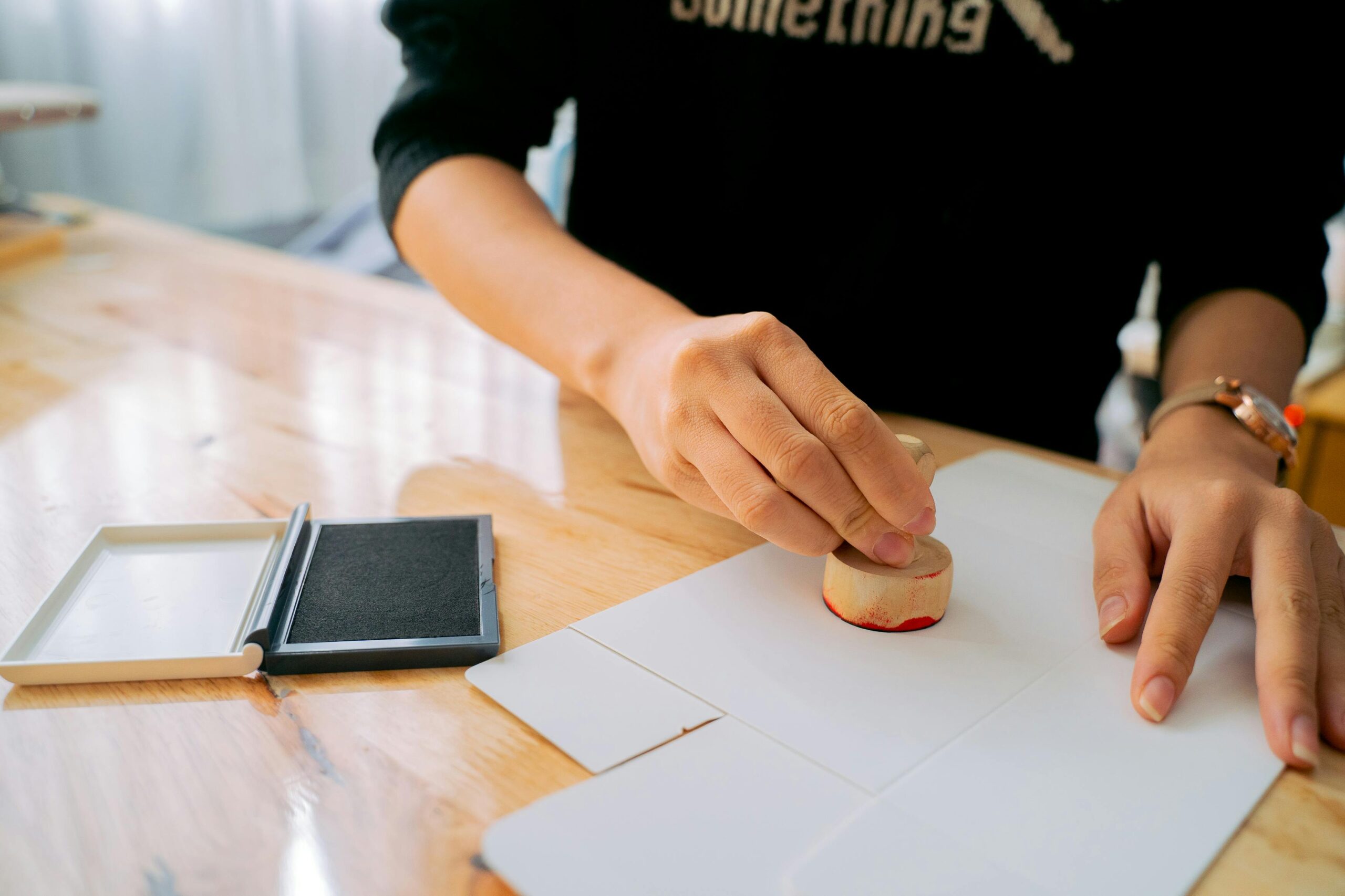 pexels-photo-6358840-6358840 Close-up of hands stamping a document on a wooden desk indoors.
